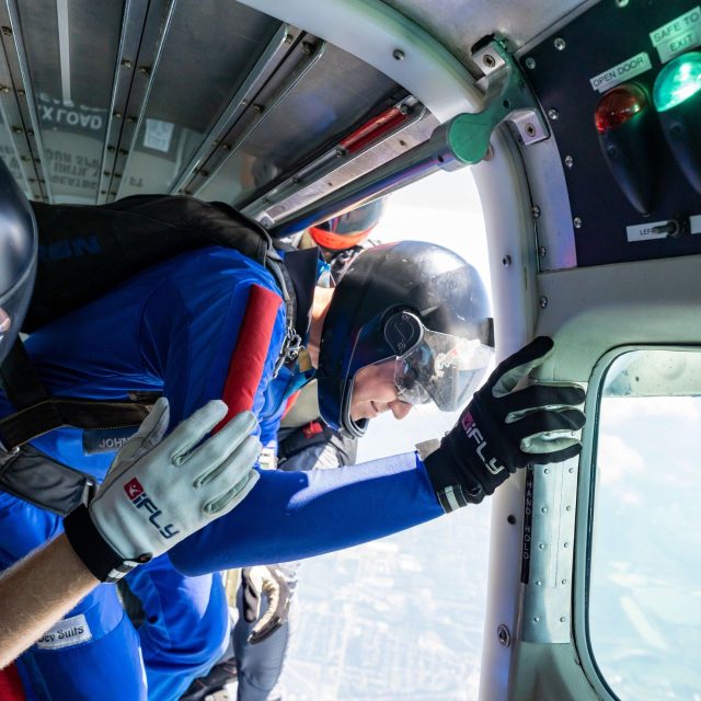 An AFF Student sets up in the door of the aircraft with an instructor on either side as the greenlight illuminates in the aircraft