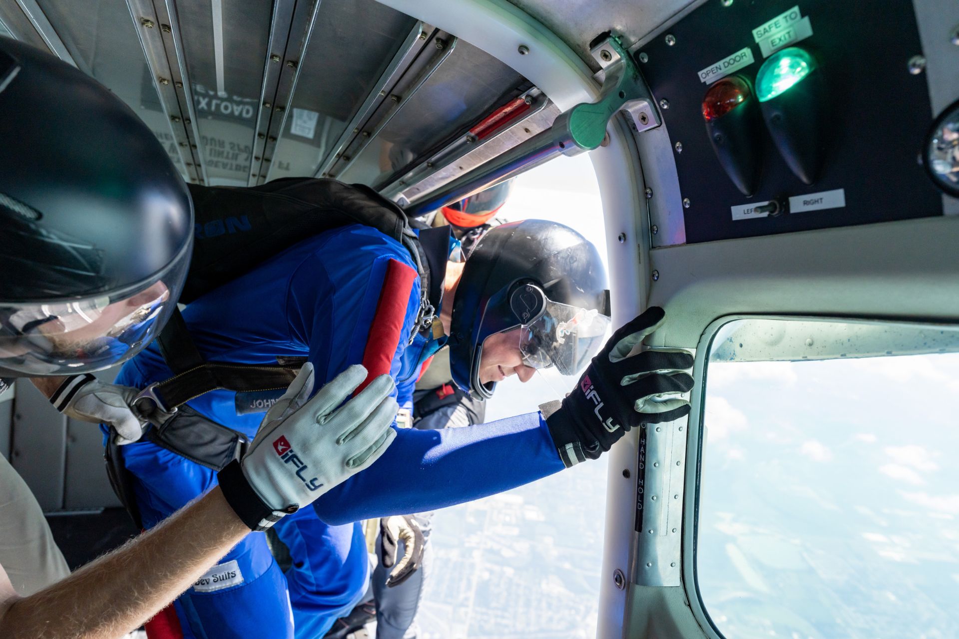 An AFF Student sets up in the door of the aircraft with an instructor on either side as the greenlight illuminates in the aircraft