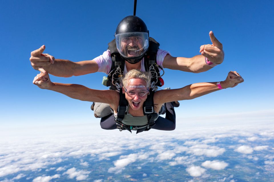 Tandem woman and her male instructor with arms outstretched during freefall.
