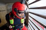 Male licensed jumper in a red helmet with a lime green and red skydiving rig gazes out the clear door of the airplane.