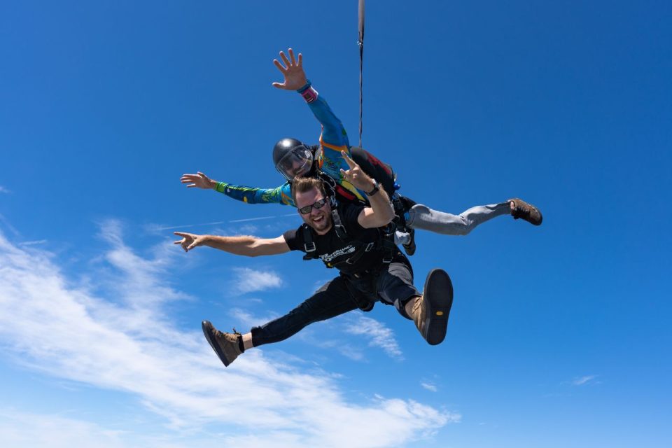Male tandem skydiving pair smiling in the air.