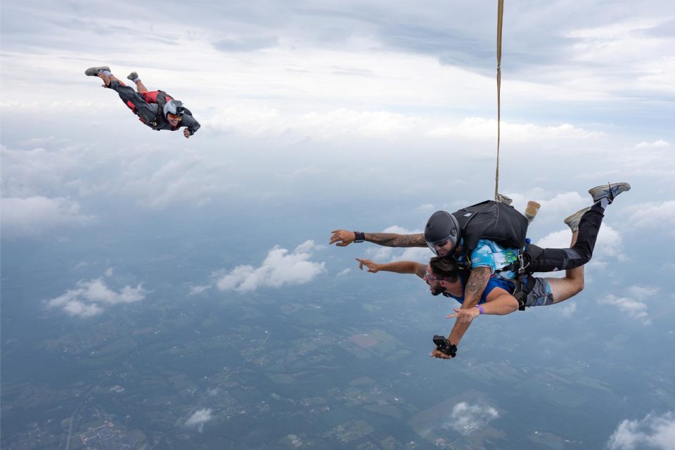 A skydiving videographer flying in freefall to film a tandem student and instructor enjoying skydiving in Cincinnati.