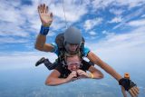 Blonde female tandem student forming a heart with her hands as she freefalls on a tandem skydive at Start Skydiving