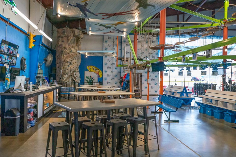 Inside Start Skydiving depicts a climbing wall, neon green ropes course, and tall tables for sitting.