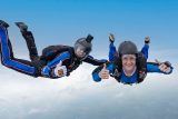 Skydiving student and her instructor give a thumbs up to the camera during freefall.