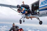 Tandem instructor and student exiting the aircraft while their talented videographer backflies beneath them to get the perfect shot