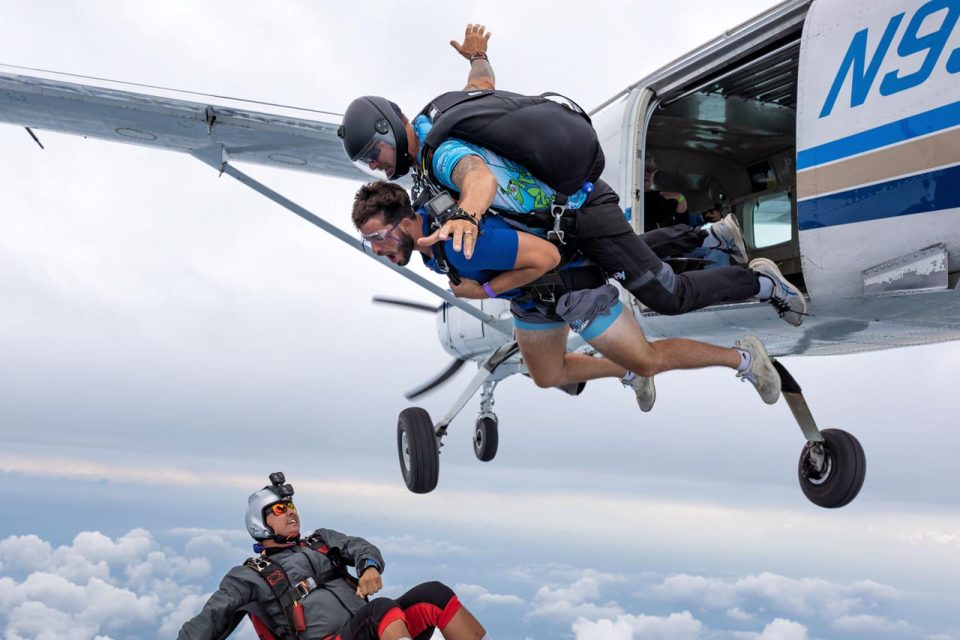 Tandem instructor and student exiting the aircraft while their talented videographer backflies beneath them to get the perfect shot