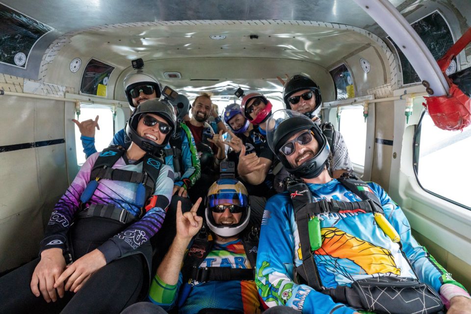 Group of licensed jumpers pose for the camera with smiles and various hand signals on the plane.