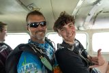 Male tandem skydiving pair with brown hair giving the shaka hand sign in the airplane on the way to altitude.