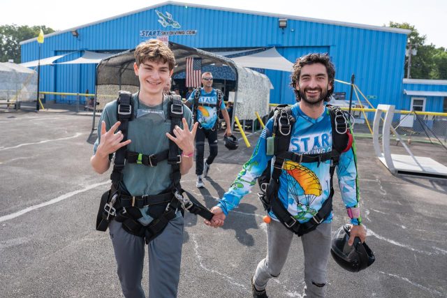 Tandem instructor leads his student to the airplane by holding on to his harness.