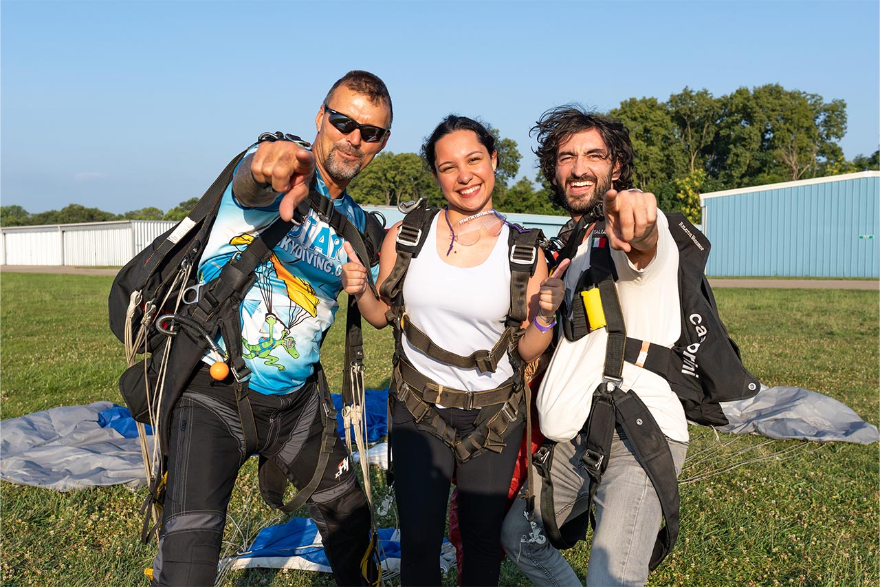 Brunette female tandem student posing with her tandem instructor and videographer after landing